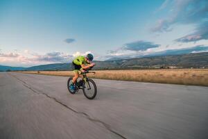 Triathlete riding his bicycle during sunset, preparing for a marathon. The warm colors of the sky provide a beautiful backdrop for his determined and focused effort. photo