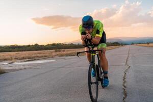 Triathlete riding his bicycle during sunset, preparing for a marathon. The warm colors of the sky provide a beautiful backdrop for his determined and focused effort. photo