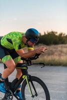 Triathlete riding his bicycle during sunset, preparing for a marathon. The warm colors of the sky provide a beautiful backdrop for his determined and focused effort. photo