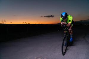A triathlete rides his bike in the darkness of night, pushing himself to prepare for a marathon. The contrast between the darkness and the light of his bike creates a sense of drama and highlights the photo