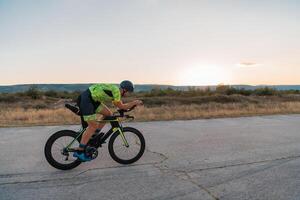 Triathlete riding his bicycle during sunset, preparing for a marathon. The warm colors of the sky provide a beautiful backdrop for his determined and focused effort. photo