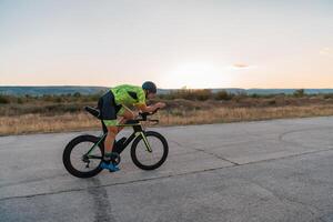 Triathlete riding his bicycle during sunset, preparing for a marathon. The warm colors of the sky provide a beautiful backdrop for his determined and focused effort. photo