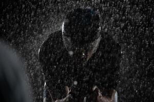 A triathlete braving the rain as he cycles through the night, preparing himself for the upcoming marathon. The blurred raindrops in the foreground and the dark, moody atmosphere in the background add photo