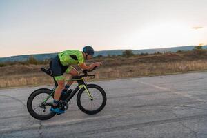 Triathlete riding his bicycle during sunset, preparing for a marathon. The warm colors of the sky provide a beautiful backdrop for his determined and focused effort. photo