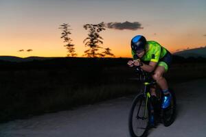 A triathlete rides his bike in the darkness of night, pushing himself to prepare for a marathon. The contrast between the darkness and the light of his bike creates a sense of drama and highlights the photo