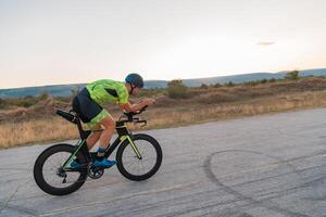 Triathlete riding his bicycle during sunset, preparing for a marathon. The warm colors of the sky provide a beautiful backdrop for his determined and focused effort. photo