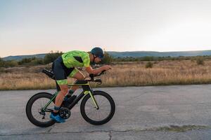 Triathlete riding his bicycle during sunset, preparing for a marathon. The warm colors of the sky provide a beautiful backdrop for his determined and focused effort. photo