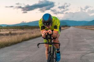 Triathlete riding his bicycle during sunset, preparing for a marathon. The warm colors of the sky provide a beautiful backdrop for his determined and focused effort. photo