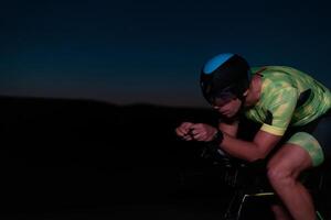 A triathlete rides his bike in the darkness of night, pushing himself to prepare for a marathon. The contrast between the darkness and the light of his bike creates a sense of drama and highlights the photo