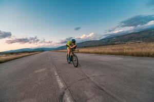 Triathlete riding his bicycle during sunset, preparing for a marathon. The warm colors of the sky provide a beautiful backdrop for his determined and focused effort. photo