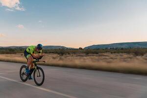 Triathlete riding his bicycle during sunset, preparing for a marathon. The warm colors of the sky provide a beautiful backdrop for his determined and focused effort. photo