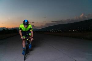 A triathlete rides his bike in the darkness of night, pushing himself to prepare for a marathon. The contrast between the darkness and the light of his bike creates a sense of drama and highlights the photo