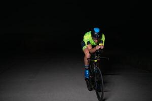 A triathlete rides his bike in the darkness of night, pushing himself to prepare for a marathon. The contrast between the darkness and the light of his bike creates a sense of drama and highlights the photo