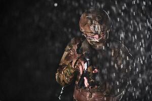 Army soldier in Combat Uniforms with an assault rifle, plate carrier and combat helmet going on a dangerous mission on a rainy night. photo