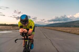 Triathlete riding his bicycle during sunset, preparing for a marathon. The warm colors of the sky provide a beautiful backdrop for his determined and focused effort. photo