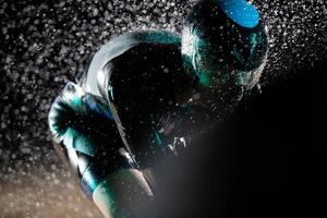 A triathlete braving the rain as he cycles through the night, preparing himself for the upcoming marathon. The blurred raindrops in the foreground and the dark, moody atmosphere in the background add photo