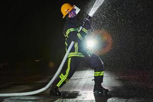 Firefighter using a water hose to eliminate a fire hazard. Team of firemen in the dangerous rescue mission. photo