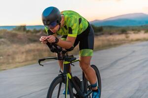 Close up photo of triathlete riding his bicycle during sunset, preparing for a marathon. The warm colors of the sky provide a beautiful backdrop for his determined and focused effort.
