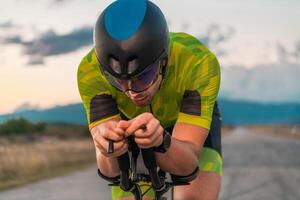 Close up photo of triathlete riding his bicycle during sunset, preparing for a marathon. The warm colors of the sky provide a beautiful backdrop for his determined and focused effort.
