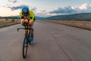 Triathlete riding his bicycle during sunset, preparing for a marathon. The warm colors of the sky provide a beautiful backdrop for his determined and focused effort. photo
