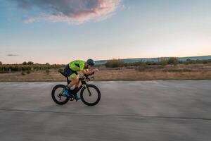 Triathlete riding his bicycle during sunset, preparing for a marathon. The warm colors of the sky provide a beautiful backdrop for his determined and focused effort. photo