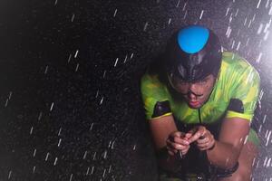 A triathlete braving the rain as he cycles through the night, preparing himself for the upcoming marathon. The blurred raindrops in the foreground and the dark, moody atmosphere in the background add photo