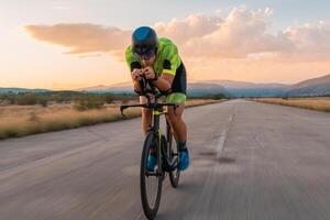 Triathlete riding his bicycle during sunset, preparing for a marathon. The warm colors of the sky provide a beautiful backdrop for his determined and focused effort. photo