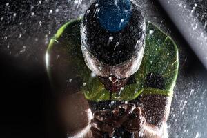 A triathlete braving the rain as he cycles through the night, preparing himself for the upcoming marathon. The blurred raindrops in the foreground and the dark, moody atmosphere in the background add photo