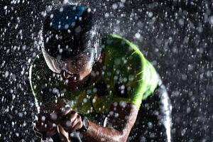 A triathlete braving the rain as he cycles through the night, preparing himself for the upcoming marathon. The blurred raindrops in the foreground and the dark, moody atmosphere in the background add photo