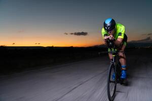 A triathlete rides his bike in the darkness of night, pushing himself to prepare for a marathon. The contrast between the darkness and the light of his bike creates a sense of drama and highlights the photo