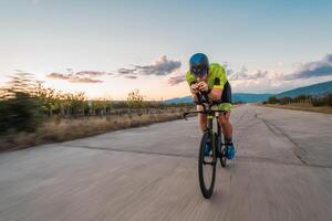 Triathlete riding his bicycle during sunset, preparing for a marathon. The warm colors of the sky provide a beautiful backdrop for his determined and focused effort. photo