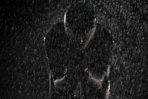 A triathlete braving the rain as he cycles through the night, preparing himself for the upcoming marathon. The blurred raindrops in the foreground and the dark, moody atmosphere in the background add photo