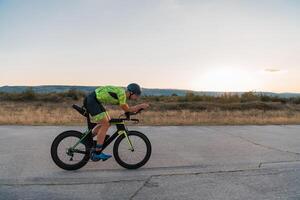 Triathlete riding his bicycle during sunset, preparing for a marathon. The warm colors of the sky provide a beautiful backdrop for his determined and focused effort. photo