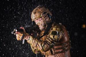Army soldier in Combat Uniforms with an assault rifle, plate carrier and combat helmet going on a dangerous mission on a rainy night. photo