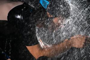 A triathlete braving the rain as he cycles through the night, preparing himself for the upcoming marathon. The blurred raindrops in the foreground and the dark, moody atmosphere in the background add photo