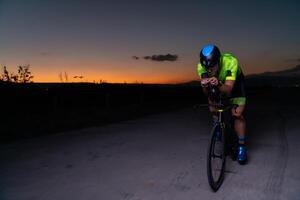A triathlete rides his bike in the darkness of night, pushing himself to prepare for a marathon. The contrast between the darkness and the light of his bike creates a sense of drama and highlights the photo