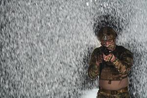 Army soldier in Combat Uniforms with an assault rifle, plate carrier and combat helmet going on a dangerous mission on a rainy night. photo