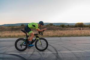 Triathlete riding his bicycle during sunset, preparing for a marathon. The warm colors of the sky provide a beautiful backdrop for his determined and focused effort. photo