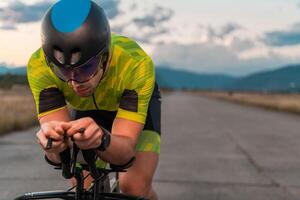 Close up photo of triathlete riding his bicycle during sunset, preparing for a marathon. The warm colors of the sky provide a beautiful backdrop for his determined and focused effort.