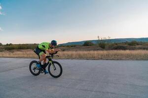 Triathlete riding his bicycle during sunset, preparing for a marathon. The warm colors of the sky provide a beautiful backdrop for his determined and focused effort. photo