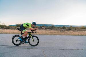 Triathlete riding his bicycle during sunset, preparing for a marathon. The warm colors of the sky provide a beautiful backdrop for his determined and focused effort. photo