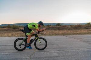 Triathlete riding his bicycle during sunset, preparing for a marathon. The warm colors of the sky provide a beautiful backdrop for his determined and focused effort. photo