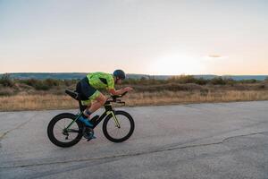Triathlete riding his bicycle during sunset, preparing for a marathon. The warm colors of the sky provide a beautiful backdrop for his determined and focused effort. photo