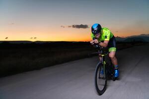 A triathlete rides his bike in the darkness of night, pushing himself to prepare for a marathon. The contrast between the darkness and the light of his bike creates a sense of drama and highlights the photo