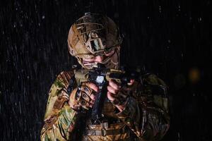 Army soldier in Combat Uniforms with an assault rifle, plate carrier and combat helmet going on a dangerous mission on a rainy night. photo