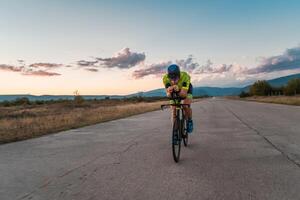 Triathlete riding his bicycle during sunset, preparing for a marathon. The warm colors of the sky provide a beautiful backdrop for his determined and focused effort. photo