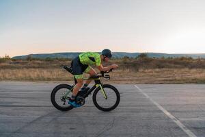 Triathlete riding his bicycle during sunset, preparing for a marathon. The warm colors of the sky provide a beautiful backdrop for his determined and focused effort. photo