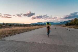 Triathlete riding his bicycle during sunset, preparing for a marathon. The warm colors of the sky provide a beautiful backdrop for his determined and focused effort. photo
