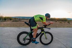 Triathlete riding his bicycle during sunset, preparing for a marathon. The warm colors of the sky provide a beautiful backdrop for his determined and focused effort. photo