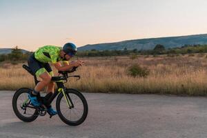 Triathlete riding his bicycle during sunset, preparing for a marathon. The warm colors of the sky provide a beautiful backdrop for his determined and focused effort. photo